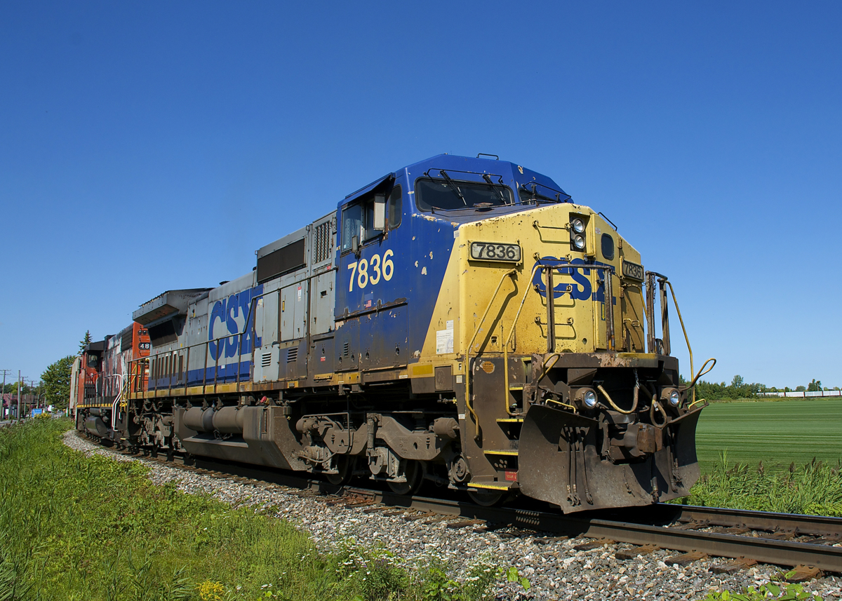 The paint on both Dash8-40CW CSXT 7836 and GP38-2W CN 4809 has seen better days as they lead a 46-car CN 327 off the Kingston Sub and onto the Valleyfield Sub, with loaded centrebreams with export lumber at the tail end barely visible at far right.