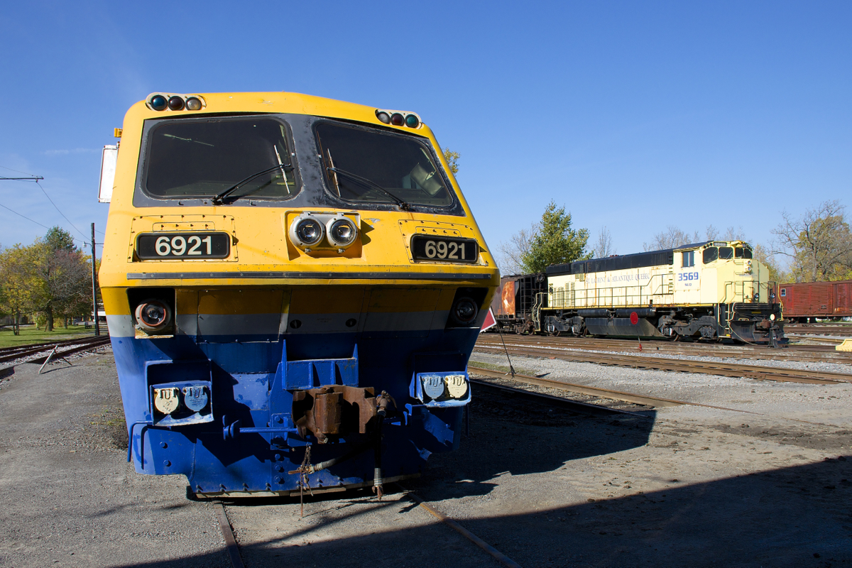 The noses of LRC-3 VIA 6921 and M-420W SLQ 3569 are illuminated in the midday sun at Exporail.