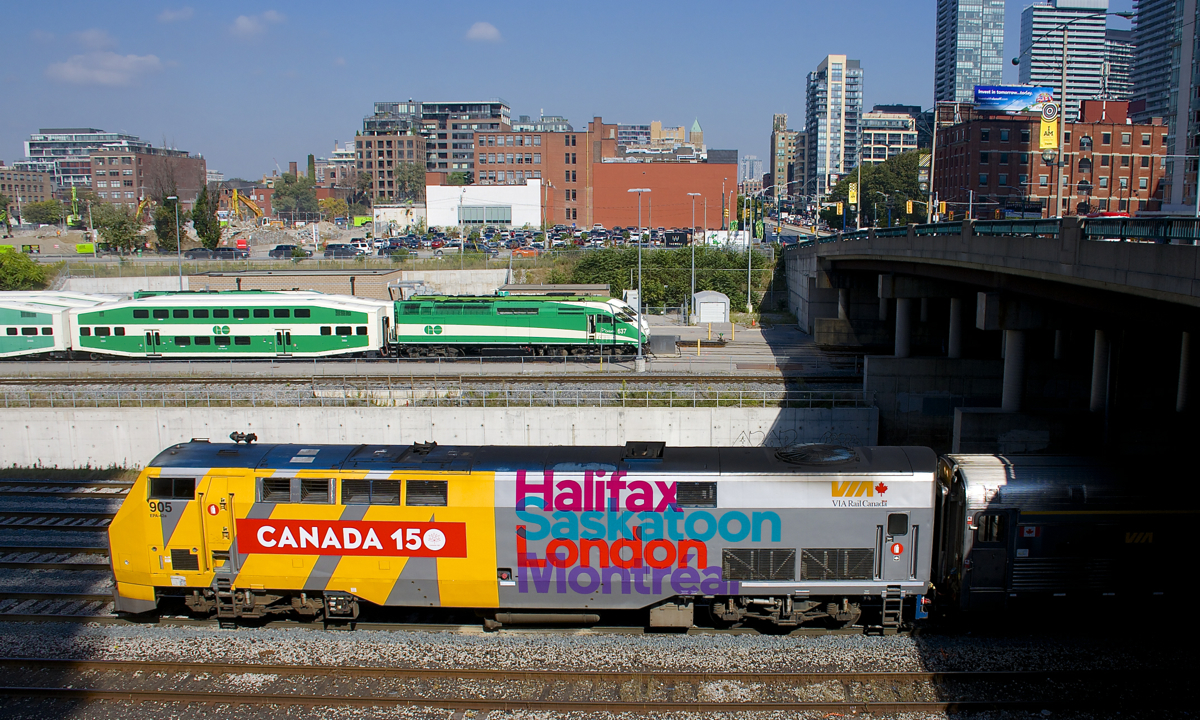 Wrapped VIA 905 pushes VIA 73 towards Union Station in Toronto. Behind is the GO North Bathurst Yard where numerous trainsets wait out the middle of the day and at right is the Spadina overpass.