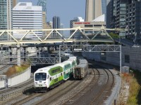 A GO Transit and a VIA Rail train are both heading east towards Union Station as they pass under an older signal bridge with classic searchlight signals. At left is a new signal bridge, not yet in use.