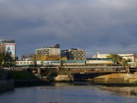 With purple-tinged clouds in the background, VIA 6446 leads VIA 33 from Quebec City over the Lachine Canal and past Wellington Tower.