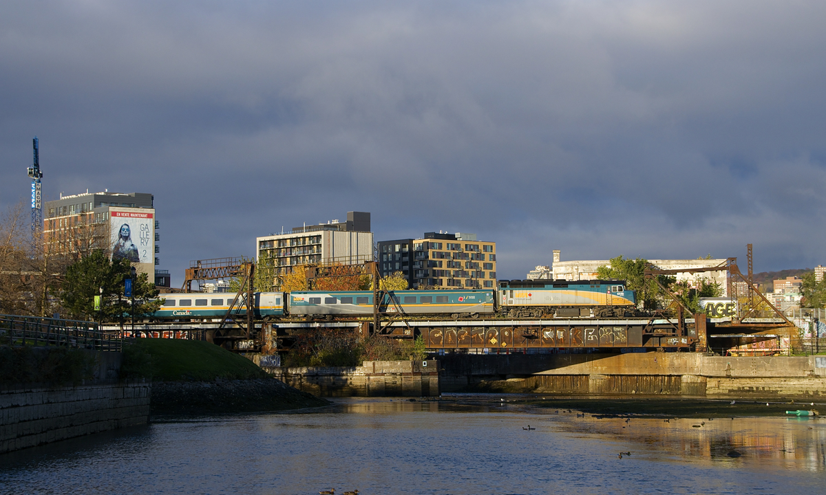 With purple-tinged clouds in the background, VIA 6446 leads VIA 33 from Quebec City over the Lachine Canal and past Wellington Tower.