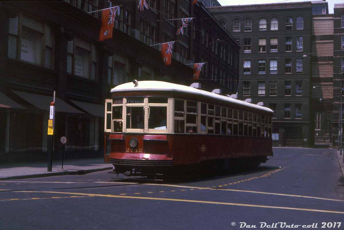 In the Shadow of Giants: TTC Peter Witt streetcar 2742 operates on a Private trip, turning at "City Hall Loop" in 1963, which consisted of track looping from Bay onto streets Louisa, James and Albert. The early-mid 1960's spelled the end of the already decimated Peter Witt streetcars in regular service on the TTC, due to the opening of the University subway line. Fantrips by enthusiasts and railway societies were common, often times chartering multiple cars.

Car 2742 is shown here turning south off James St. to west on Albert St., amidst the towering department store, warehouse and manufacturing buildings of the T. Eaton Co., no doubt decked out to the 9's for Dominion Day on July 1st (Canada Day) in typical Eatons fashion. A Canadian icon and retailing powerhouse, Eatons had in the works at the time plans to buy up and redevelop this whole area into a new Eaton's development, replacing the Queen Street store, all of its old manufacturing, retail and warehousing buildings in this block, and even Trinity Church and Toronto's Old City Hall with a new modern department store, office towers, a hotel and the works. City and residential opposition quashed the plan after several years and nothing became of it. Eaton's later came back to the table in the 70's with a new proposal, that eventually became the modern-day Eaton Centre. The streetcar tracks here, the old towering buildings surrounding them, and a number of small side streets were casualties of the new development, and eventually changing times and a failure to "mind the store" would catch up with Eatons in the end. Like the Peter Witt cars that were once so common - here today, gone tomorrow.

F.H.Worsfold photo, Kodachrome from the Dan Dell'Unto collection.