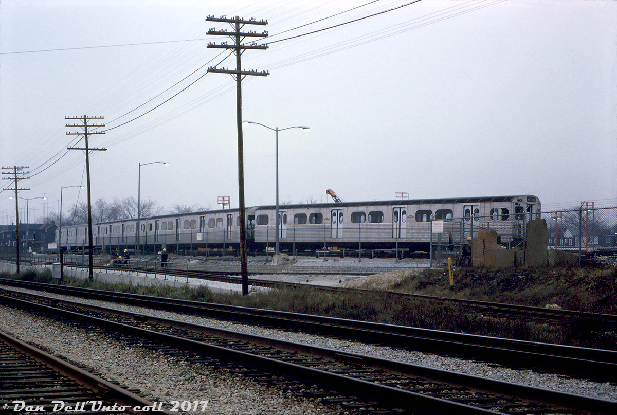 A 4-car set of Montreal Locomotive Works (MLW) built "M1" subway cars sits at the back of the TTC's new Greenwood Yard in storage, as viewed from CN's Kingston Sub mainline to the south. Greenwood Yard was built in the 1960's in Toronto's east end to store, maintain and service trains on the under-construction Bloor-Danforth subway line. The opening of the B-D line was still 3 months away (February 1966), and Greenwood wasn't fully operating yet, but since May it had been taking deliveries by rail of new H1 subway cars that would provide service on the line.

The M1's (numbered 5300-5335) were the first new subway cars built in Canada, and featured a 75-foot light-weight aluminum bodied design that's basically still the standard for new TTC subway cars today (compared to the original steel 57' "Red Rocket" Gloucester cars made in the UK). They were built a few years earlier to serve on the then-new University subway line. MLW only got one order from the TTC in the early 60's, all subsequent orders of the same design went to Hawker Siddeley Canada (H1, H2, etc). Due to their historical significance, the first two cars of this order (M1's 5300 & 5301) were donated to the Halton County Radial Railway museum for preservation when the series were being retired in the late 90's.

The standard-gauge railway siding (or spur) into the yard had two legs that formed a C-shape, visible in this photo and in aerial imagery. The western leg went to the unloading ramp that was used to unload new subway cars that were delivered by rail flatcar. Another siding looped up by one of buildings on the south-east side (perhaps for delivering materials). The first deliveries by rail here were the H1 cars in 1965, and the final ones were apparently the T1's in the late 90's/early 2000's. Some of the siding is still intact but out of use (with the switch to the mainline removed), and all current subway car deliveries are trucked down from Bombardier in Thunder Bay.

Robert D. McMann photo (slide unnamed, but likely), Kodachrome from the Dan Dell'Unto collection.
