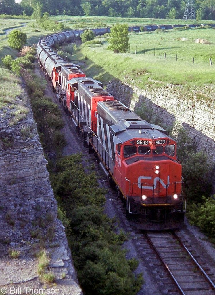 A trio of GP40-2Ws lead by CN 9633 handle an oil train to Lennox Generating Station, backing up the 5.6 miles to the hydro plant as seen from the County Road 22 bridge over the spur about a mile south of the Kingston Sub, on June 11th 1992. At that time both oil and natural gas were being used depending on price.