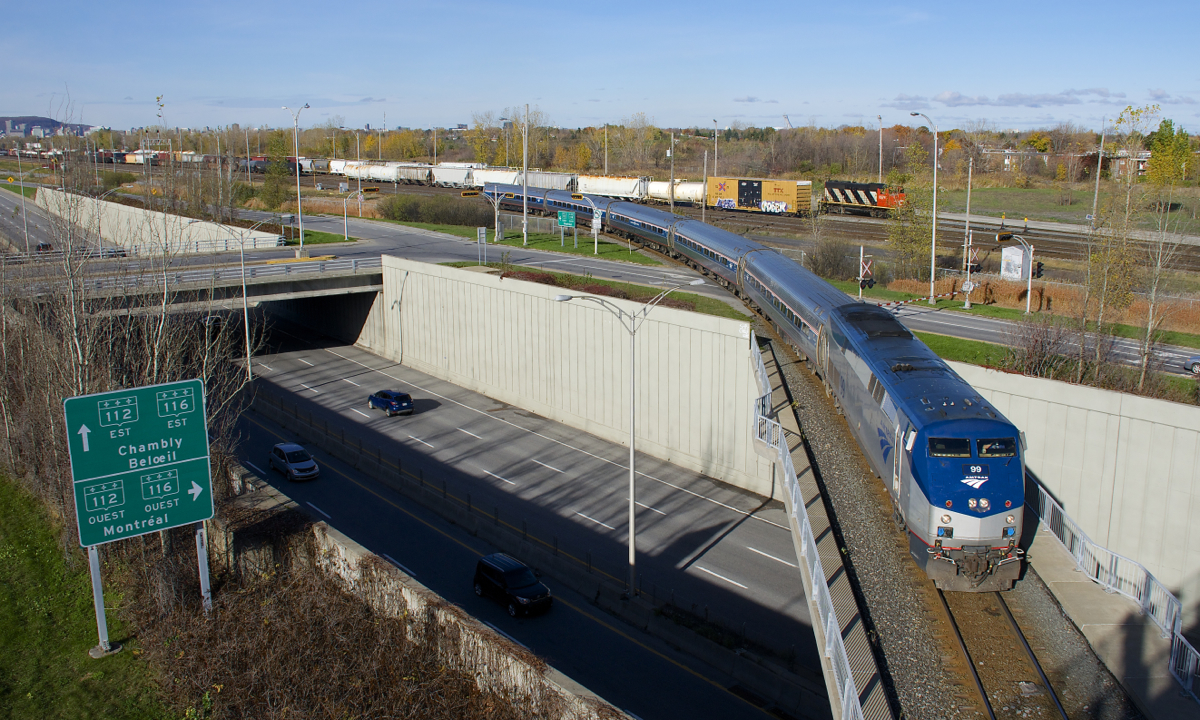 Amtrak's Adirondack is leaving CN's St-Hyacinthe Sub and taking the the Rouses Point Sub as it crosses over Route 116. In the background is Southwark Yard, including CN 9576, which is switching CN 522.