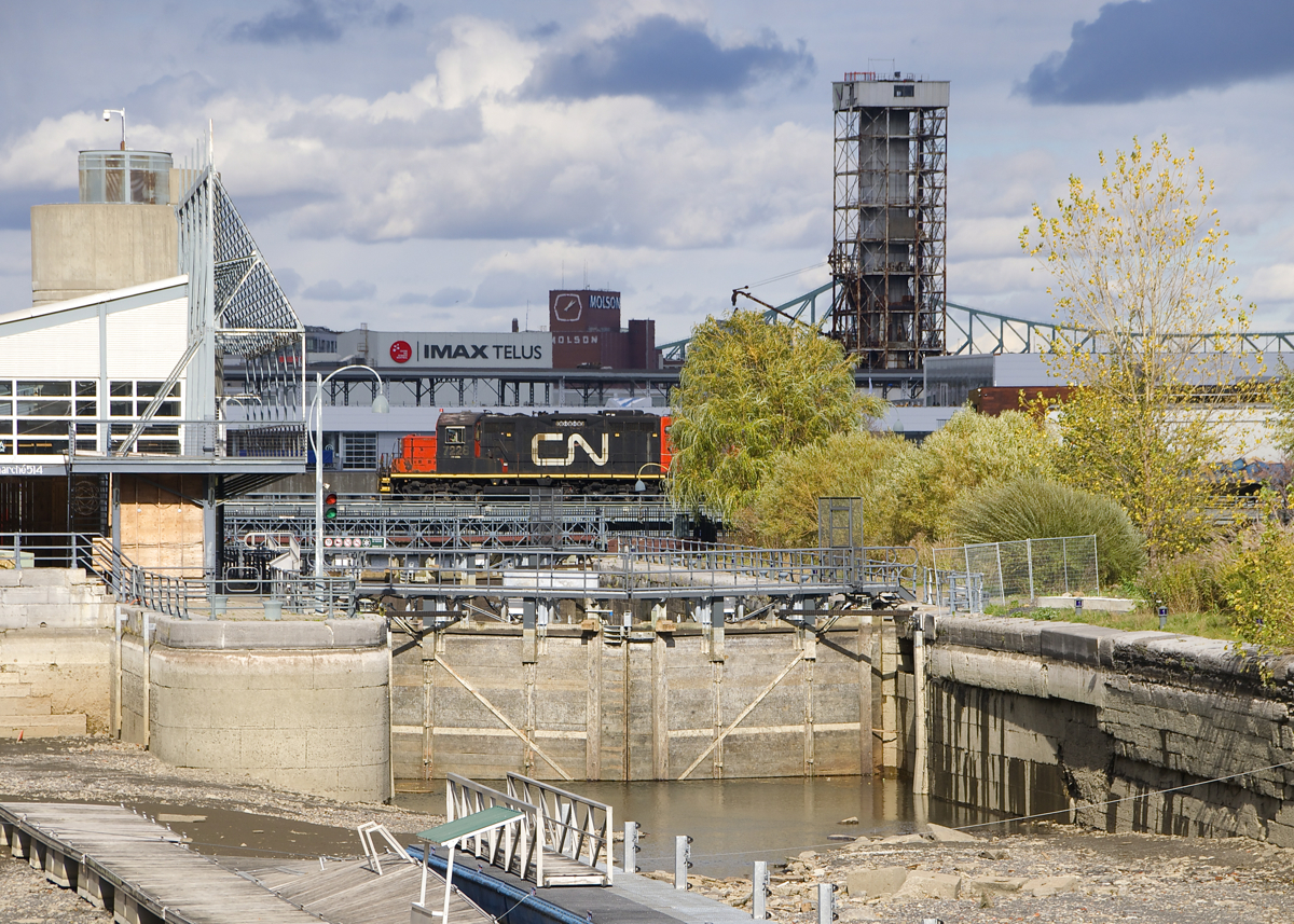 As happens every fall, the Lachine Canal has been mostly drained, as CN 7228 stops on a bridge over the canal. Soon it will back up towards Bickerdike Pier with a cut of grain cars.