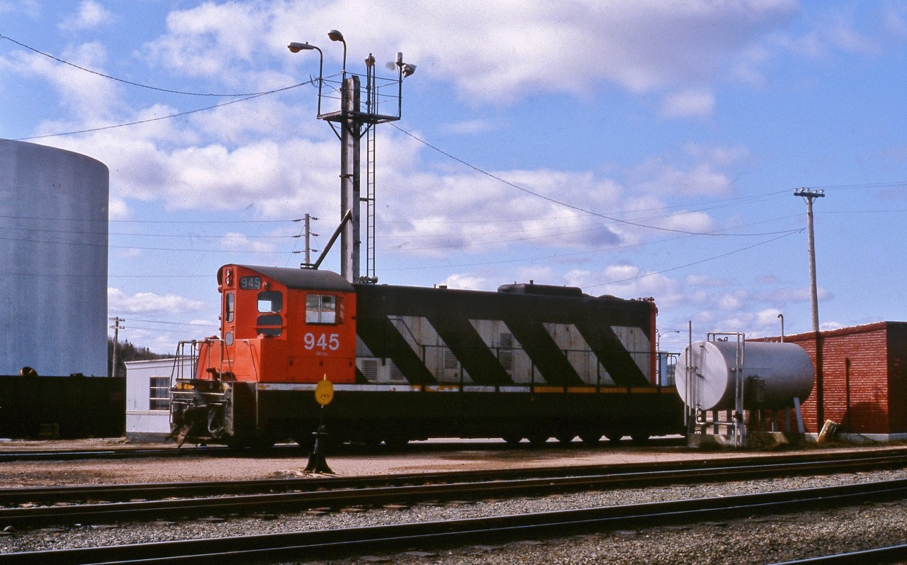 DIESEL DEPARTURE. NF210 # 945 is refuelled just prior to departure as the only unit on Terra Transport's Mixed Extra 945 West on April 20, 1987. This was the photographer and his girlfriend's (now wife) first ever trip on a Newfoundland train and the two would be the only passengers to travel the entire 138 miles in Coach 757 from Bishops Falls to Corner Brook that day. Narrow gauge unit # 945 was the second last in an order of 9 such 1200 horsepower units built by GMD to be delivered to the CNR's Newfoundland Division in 1960. Due to the excellent maintenance carried out by the shop crews after 28 years of service, it would be later sold to the F.C.A.B in Chile in 1988.