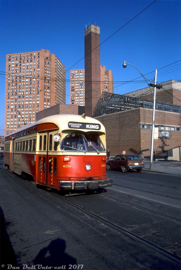 After departing Dundas West Subway Station and crossing Bloor Street, TTC PCC 4356 operates on an eastbound King run heading south on Dundas Street, passing Bishop Marrocco Secondary School and The Crossways Mall towers. Both still serve as landmarks at the busy Dundas-Bloor intersection today, which got even busier with the opening of the Union-Pearson Express (that stops a stones' throw away at Bloor GO/UPX Station). 

Note the water bumpers outfitted to 4356. The TTC outfitted various buses and streetcars with them starting in 1969, basically rubber sacks filled with a liquid saline solution that would pop out of plugs at the top during a collision and help absorb the impact (they were apparently phased out after it was found they were causing corrosion to the carbodies). Our intrepid and unknown photographer is visible at the bottom, no doubt bundled up well on this December afternoon. And yes, that appears to be an early Honda Civic parked out front (a brown 70's hatchback version). You probably won't find too many of those around these parts today, as those early Japanese cars were known to eventually rust to pieces after facing the usual Canadian winters.

Original photographer unknown, Kodachrome from the Dan Dell'Unto coll.