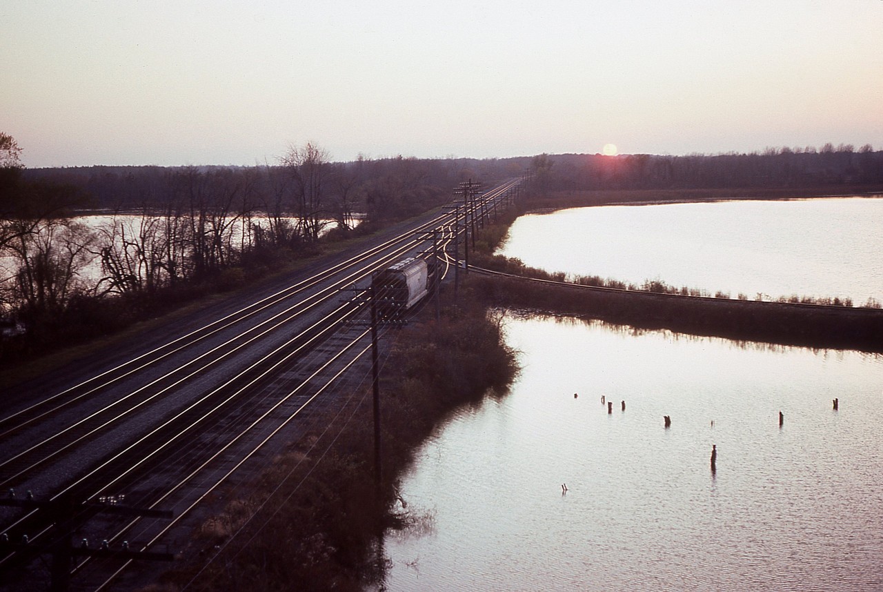 Sunset on the 'Great Raceway'. As of this photo date the CASO was still under control of Consolidated Rail as their CDN Northern Region 'showpiece'.  The line was dissolved into the control of CN and CP a couple of years later. In this view at end of day looking west from atop the old Lake Erie & Northern trestle over the line, it is hard to believe this magnificent mainline is but a memory. Traffic is winding down, yet the ribbons of steel apparently still look well-used. The two left lines are main, the other service tracks (north side) for trains such as TH&B's Nanticoke to come off the west leg of the wye there (shown) unrestricted.
Today all the rail is gone, it is but hiking/walking paths, with controlled vehicle access for those wishing to go fishing in the Waterford Ponds, that body of water beyond the West Leg.