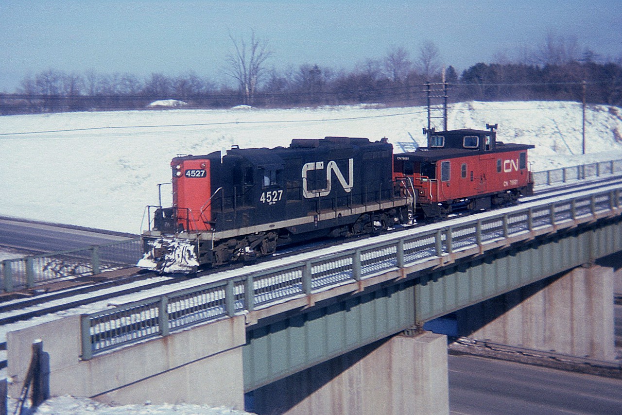 Reminiscences galore....is how I feel looking at simple images taken in simple laid-back times. A Fort Erie-based GP 4527 with van 79581 is seen on one of those pleasant sunny late mornings crossing over the Hwy 403 heading westward.  I forget, but this must be a Sunday. Note the 403 traffic below. Simple times were also quiet times. And yet, we saw far more trains.
I accessed this spot by parking at the Royal Botanical Gardens, then walking over to Hamilton West, down the hill over to CP, along the tracks to the CP bridge just to the south, which I used for crossing over the 403 and then about 60 feet N to where I am standing now. Not much ran on the CP, and when it did, it ran s-l-o-w. Much safer than getting squished on the CN. Of course, none of these antics are legal any more; just another route of wandering a thing of the past.
