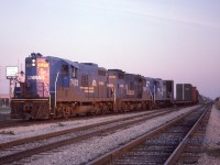 Three Canada Division GP9s (7432-7437-7434) lead a small WQST-1 off Westbound main and into the Class Yard lead at Howard Ave, Windsor Ont just before sunset on Sept 30th 1992. Normally, this train would arrive in Windsor early afternoon and would be back in St Thomas by this time. In the distance above the Eastbound main can be seen the signals at Pelton.