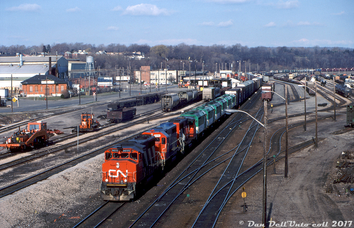 CN train #331 rolls through CN's Stuart St. Yard in Hamilton with some interesting interlopers in tow: GO Transit's entire fleet of six GMD-built F40PH locomotives, bound for their new owner Amtrak in the States. Casualties of all the new F59PH's GO acquired, former 510-515 have been retired, sold, and given their new 400-series Amtrak numbers (410-415, at the end of Amtrak's ~210 unit fleet), but not yet repainted or had their GO logos and lettering removed. The head-end consist is CN GP40-2W 9655, GTW GP40-2 6416, another unknown CN GP40-2W, and GO/Amtrak F40PH's 415, 412, 414, 411, 413 & 410.

Visible in the background are various industrial buildings that have since been leveled in recent years. No doubt Hamilton natives can point them all out, but notable are the old Canada Iron Foundries (Canron) on the left, and CN's Hamilton Express Building in the upper middle (built 1964, closed 1997, demolished 2009). The old CN diesel shop next door (teaming with switcher units) continued to be in use under Railink's Southern Ontario Railway until it too was demolished in the recent past for GO Transit service expansions.

Reg Button photo, from the Dan Dell'Unto collection.