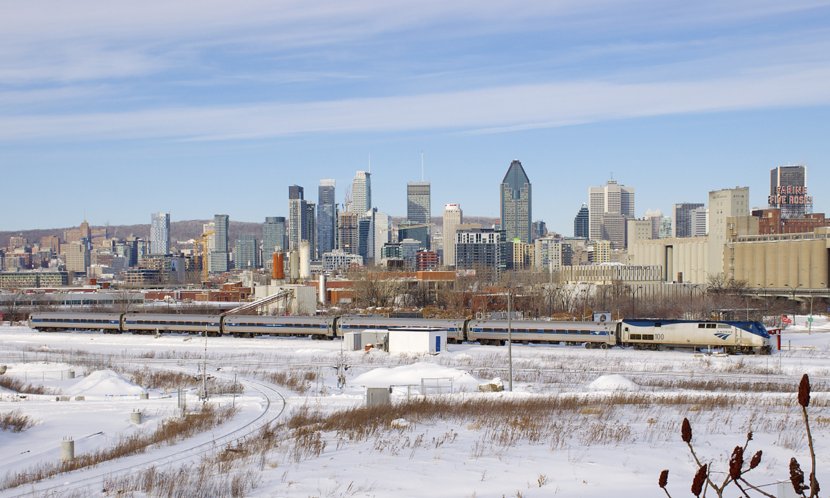 The Adirondack is leaving Montreal with AMTK 100 leading five Amfleet cars, behind the train is the skyline of downtown Montreal.