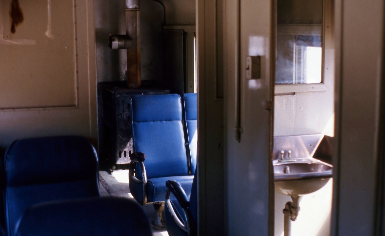 SPARTAN BUT SPECTACULAR. The sunlight reflects from what remains of the previous winter's snow through the windows of Terra Transport Coach 757 to illuminate its spartan but comfortable interior at the flag stop of Quarry. Originally built in 1943 as coach No. 40 for the Newfoundland Railway by the CC&F it was assigned to the Bishops Falls - Corner Brook run from 1984 to 1988 after the mixed runs on the branchlines were cancelled. Were it not for the excitement of the photographers and his girlfriends first run on a Newfoundland train, the radiant heat from the oil stoves (one in each end and tended to by the conductor) and the huge comfortable vinyl seats, it would be so easy to drift off to sleep with the gentle rocking and rolling of the narrow gauge train.