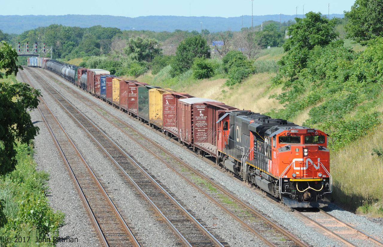 Weekend train 422 is short enough  to enter Aldershot Yard from the west end, under the CN Snake (Road) signal gantry a mile away. Less common in recent years is all-GM power, CN 8932 (SD70M-2, CN class GF-643h) leading CN 5431 (standard cab SD60 ex-EMDX/Oakway, CN class GF-638c). The Niagara escarpment is the high background.  Tip-over warnings on the lumber cars are clear, I wonder how often that happens.