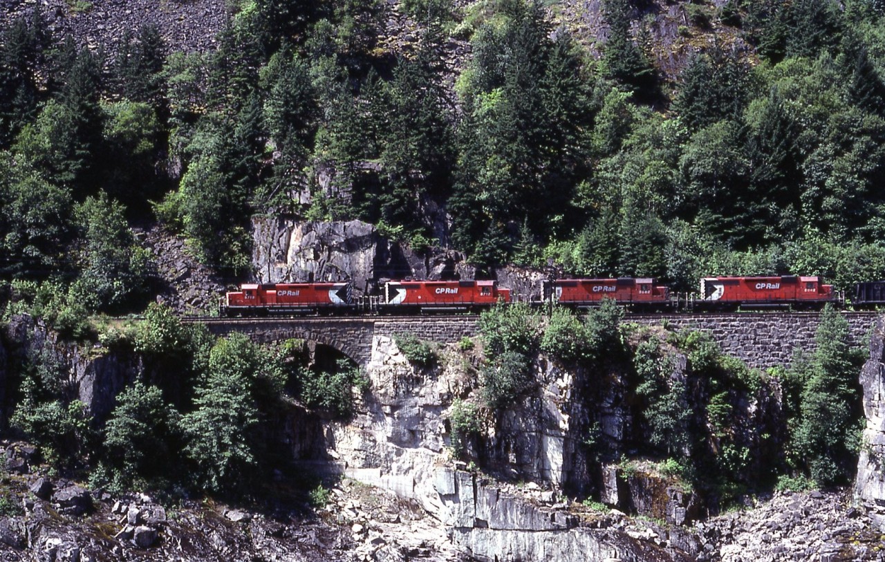 A west bound coal train headed for Roberts banks crosses just one of many stone viaducts near Hell,s Gate in the Fraser Canyon. 3 mid train helpers or slaves as known back then rounded off the power.  i had the exact location recorded, but time has misplaced it. if any one could help, please do.