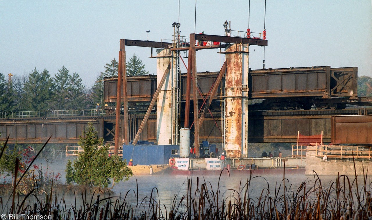 CN was replacing bridge girders over the Trent Canal and River in 1997. Seen here, a Dominion Bridge barge-mounted derrick lifts an old bridge span out onto a heavy-duty flatcar, in preparation of installing a new span in its place.

Photo of a new bridge girder span waiting to be installed, at Belleville ON: http://www.railpictures.ca/?attachment_id=31955
