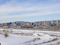 A extra section of VIA 15 with an all-stainless steel consist is passing the skyline of downtown Montreal, just after exiting the Victoria Bridge and nearly at its terminus of Central Station. Bringing up the rear is Park Car <i>Tweedsmuir Park</i>.