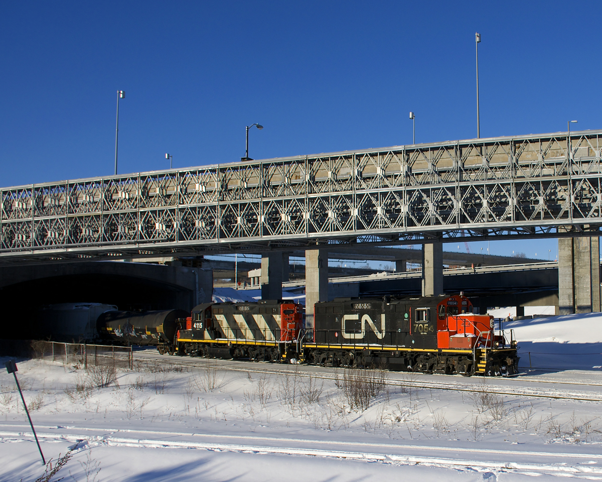 The Pointe St-Charles switcher is eastbound as it passes under the rapidly changing Turcot Interchange in Montreal with GP9's CN 7054 & CN 4115 for power and cars for Pointe St-Charles Yard.