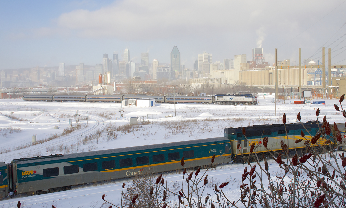 AMTK with AMTK 514 leading is about ten minutes out of Central Station in Montreal as it passes the downtown skyline. In the foreground is a very late VIA 633, preparing to head onto the Victoria Bridge before backing up to Central Station. As is the case every Sunday, it is deadheading a second consist for Ottawa.