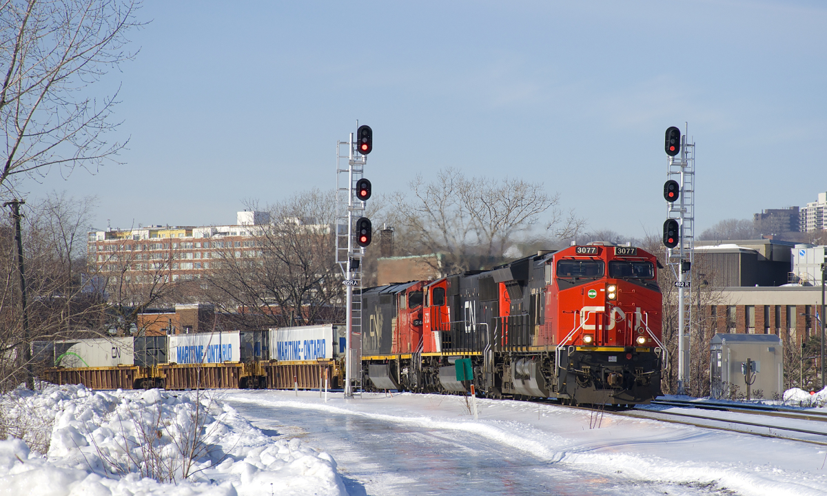 A couple of days after a large amount of freezing rain coated the remaining snow in Montreal, uncleared fields and paths are a real skating rink. Here CN 120 passes some of this ice-covered snow with CN 3077, CN 5733 & CN 2440 for power and a 514-axle long train as it splits the signals in the St-Henri neighbourhood of Montreal.