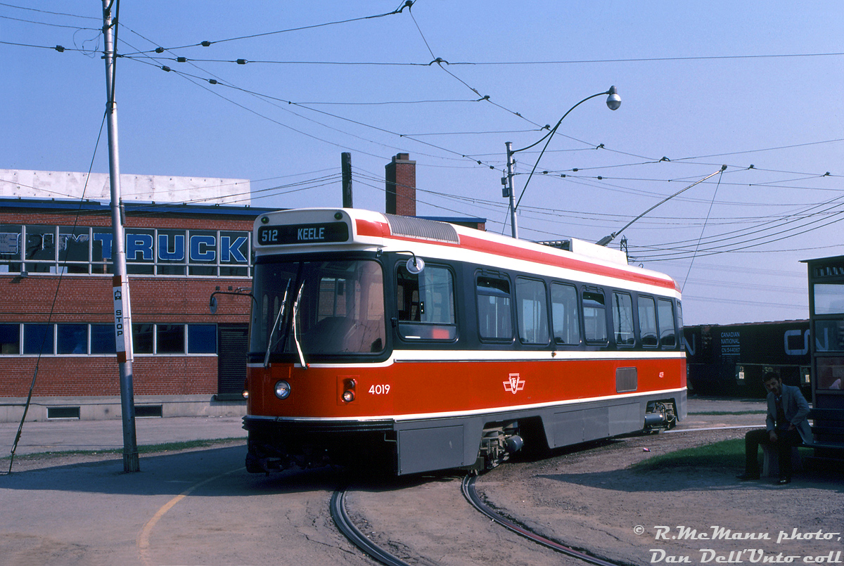 Toronto Transit Commission CLRV 4019, less than a year old and still looking factory fresh, pauses at the end of its westbound 512 St. Clair run at Keele Loop on the morning of May 4th 1980, ready to head back east. CN's West Toronto Yards can be seen off to the right, and the old car dealership behind was originally a CN Express and Telegram building (later becoming High Park Ford, then Church Motors Ford).Located just north of St. Clair Ave. W. on the east side of Weston Road, the new UTDC-built CLRV streetcars only served TTC's Keele Loop briefly. St. Clair streetcar service would be extended west to the newly constructed Maybank Loop (later renammed Gunn's Loop) to the west off St. Clair at Maybank Ave. at the end of July 1981, and Keele Loop would be closed. Presently a neighbourhood full of townhouses occupies this site.Robert D. McMann photo, Daniel Dell'Unto collection.