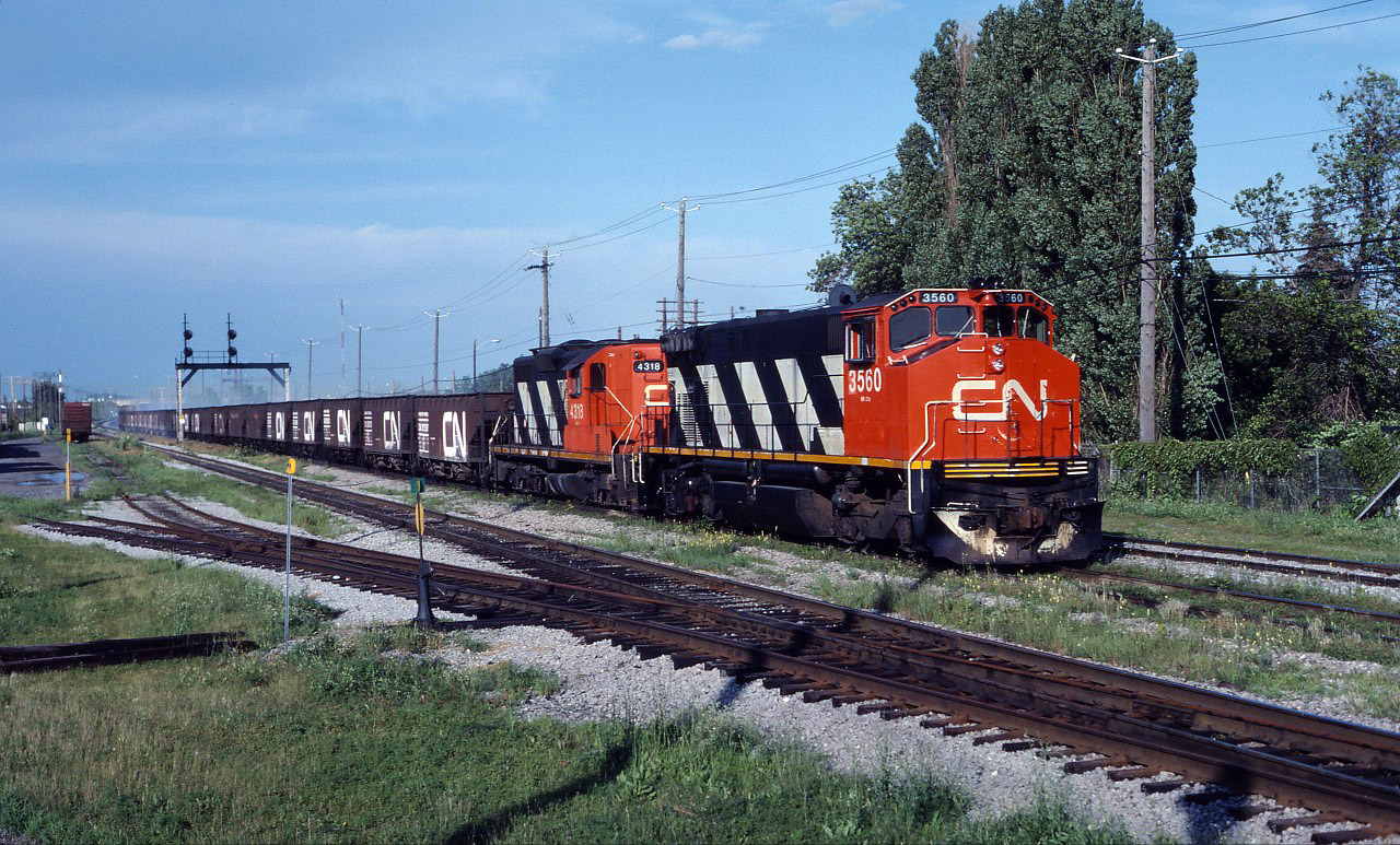 CN M420W 3560 and GP9 4318 lead a ballast train through St. Lambert on a beautiful summer evening in July 1990.