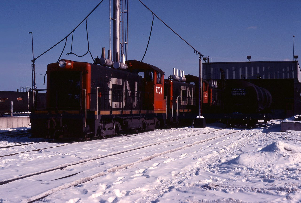 While many of us associate MLW S4 and GMD SW1200RS units with Hamilton yard duties; in the mid-1980s, 1200 hp SW9 and SW1200 units fulfilled that role (before the SW1200RSs were assigned to this service). Here we see two SW9s, 7704 and 7701, and another GM switcher on the west side of the Stuart Street diesel shop. These units have been renumbered from the 7000s, permitting GP9 units being rebuilt at that time to assume that number series. Also note the fuel delivery tank car.