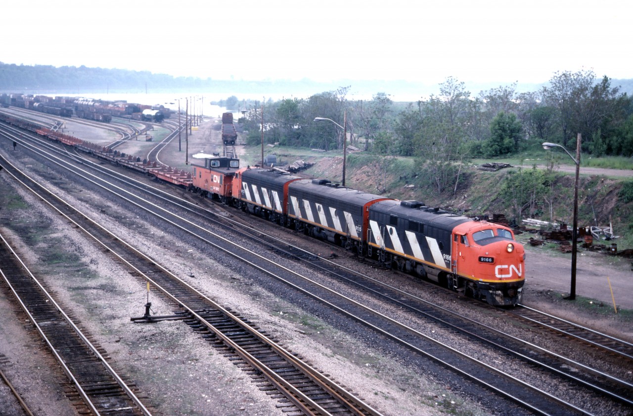 By 1986, many of CN's F7u locomotives had been displaced from service in Western Canada and migrated east. Most held assignments in southern Ontario, such as the Hamilton-Nanticoke "steel train" which regularly used an A-B-A set. Here we see 725 leaving Hamilton Yard and about to head up the Escarpment via street-running on Ferguson Avenue. The train carried two cabooses/vans to facilitate run-around moves in Nanticoke and Brantford.