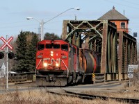 Rolling across the old swing bridge over the Kaministiquia River, utilizing power off the nights road freight from Fort Frances of SD60F 5527 and GP40-2wl 9525, the 07:30 Neebing Yard crew has grain loads for Mission Terminals Ltd and Cargill on the drawbar. There duties will be pull and spot the elevators and may have had a switch at the Bowater Sawmill, all located at the end of the spur.<br><br>This bridge is a rail/ road bridge, built by the Grand Trunk Pacific Railway in 1906. A contract was signed between the GTP and the Corporation of the Town of Fort William and a sum of $50,000 dollars was given to the railway. In return the municipality gained "the perpetual right to cross said bridge for street railway, vehicle and foot traffic on roadways supported by brackets on each side of the railway bridge." On October 29, 2013 the bridge burned, repairs were made to continue rail traffic but the bridge has since remained close to vehicle and pedestrian traffic due to a dispute between CN and the City of Thunder Bay determining who is responsible to pay for repairs. The issue had been taken to court and in June 2017 a judge ruled CN does not have to fix the bridge. The dispute continues as in August 2017 Thunder Bay appealed the decision. This is the most direct link for people commuting between the City and the Fort William First Nation.