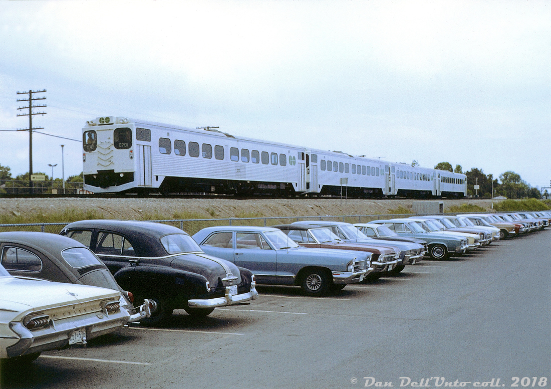 A train of GO Transit self-powered single level Hawker Siddeley cars (signed up with a "Test Train" placard at the end) heads through Guildwood GO Station passing lines of now-vintage autos parked at the station sometime in the late 1960's. To start their commuter operation, GO purchased tonnes of single level coaches & cab cars built by Hawker Siddeley Canada (based on their subway car design) for use in conventional trains with locomotives, but they also purchased 9 self-propelled versions in 1967 powered by Rolls Royce engines (all single ended RTC-85SP models, except two with cabs on both ends which were RTC-85SPD). They were intended to operate in off-peak service, but due to reliability issues were eventually de-powered and converted to regular cab cars in 1975, and lasted as such until retirement. Trailing car D701 is currently still plying the rails as Ontario Northland coach 702.

J.Woollatt photo, Dan Dell'Unto coll.