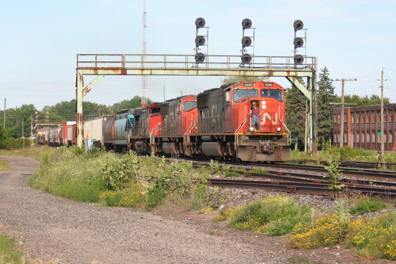 A veteran conductor on a westbound CN train comes down from his chair to confirm the approaching signal at Paris West, Ontario on the Dundas Subdivision as the high afternoon sun blazes down on his train. The elephant style consist includes; 5680/ 5738/ 2588.