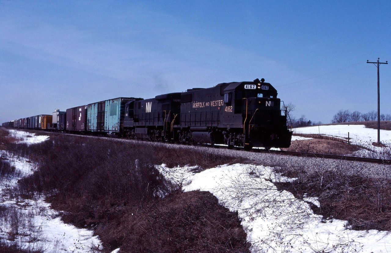 The last of the winter snow is still on the ground as an N&W eastbound moves through Cayuga behind GP38-2 4162 and C30-7 8003. Note that the class lights on the lead engine are lit white--signifying that this is an "extra" running in Manual Block System territory. Prior to the introduction of MBS in the early 1980s, eastbound trains on the Cayuga sub ran under time table schedule authority and westbounds were extras.