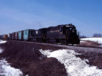 The last of the winter snow is still on the ground as an N&W eastbound moves through Cayuga behind GP38-2 4162 and C30-7 8003. Note that the class lights on the lead engine are lit white--signifying that this is an "extra" running in Manual Block System territory. Prior to the introduction of MBS in the early 1980s, eastbound trains on the Cayuga sub ran under time table schedule authority and westbounds were extras.