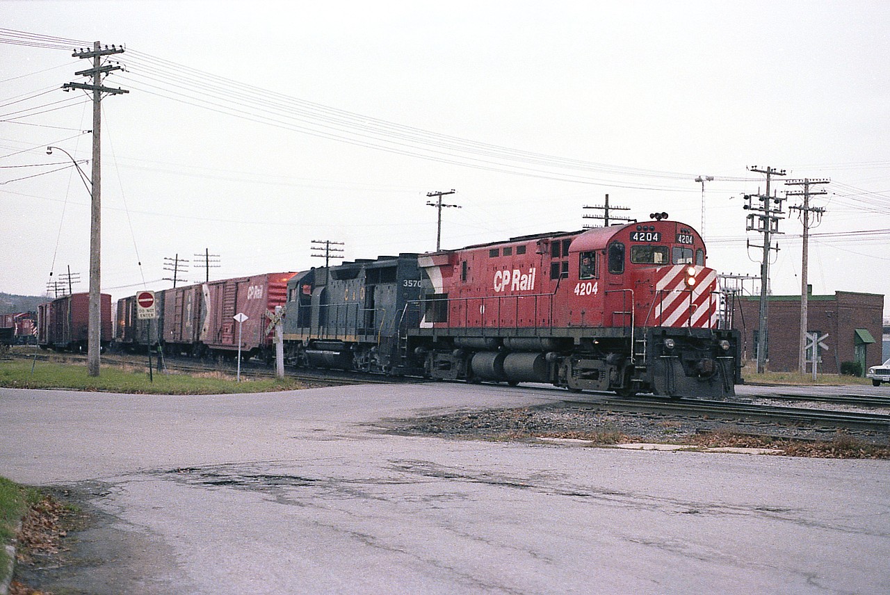 CP 4204 and C&O 3570, an eastbound freight; slows to a temporary stop at the station in Woodstock.  Just for a few moments the Ingersoll Ave crossing is fouled before the train moves on. This is nearly 40 years ago; today this same location is well protected with flashing lights and barriers. Track configuration has changed a lot as well.