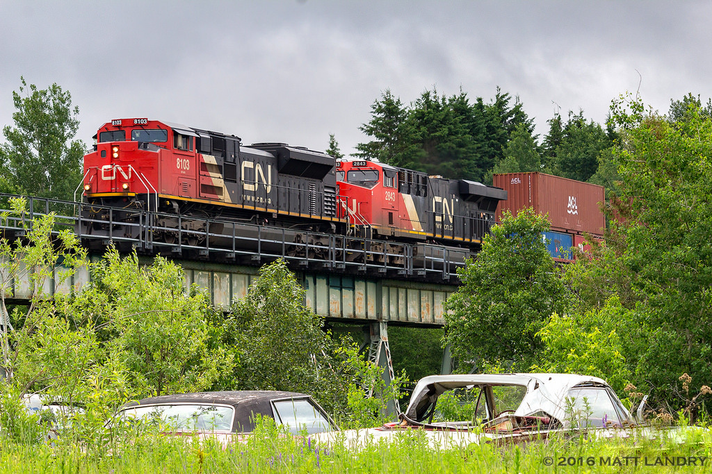 CN 8103 leads stack train Q121, heading over a small trestle shortly after passing through the town of Grand Falls, New Brunswick.