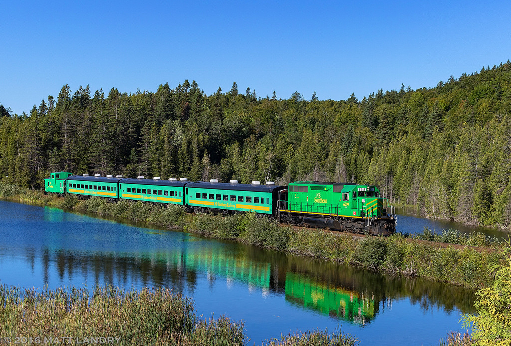 NBSR 6319 leads a passenger train along the CN Sussex Sub towards Renforth, New Brunswick, for the Dragon Boat Festival. They make three trips from Harbour Station in Saint John to Renforth, then make three trips in the afternoon to pick up passengers to head back to Saint John. Seen here, passing by the "unnamed lake". True story.