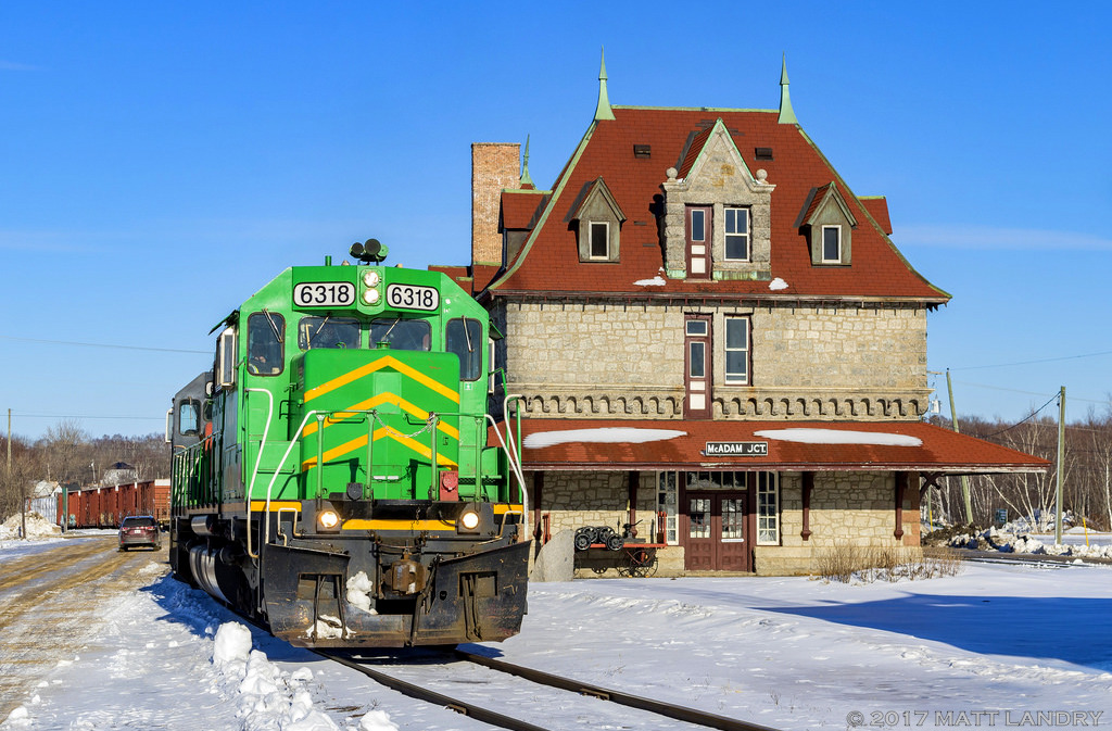 NBSR 6318 leads a New Brunswick Southern Railway westbound freight, as they pull by the famous railway station at McAdam, New Brunswick. They crew will pull ahead, set off a couple of cars in the yard. Then a new crew will take over and bring the train westward into Maine.