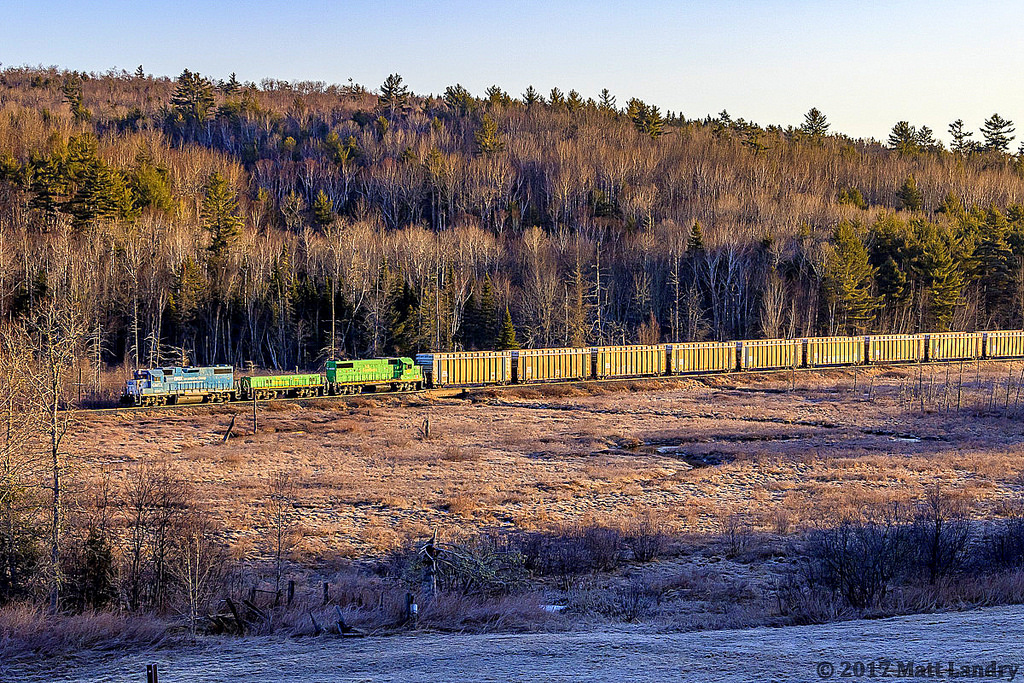GMTX 2233 leads a New Brunswick Southern Railway "X907" empty woodchip train westbound at Clarendon, New Brunswick, with the rising sun shining some nice light along the chip cars.