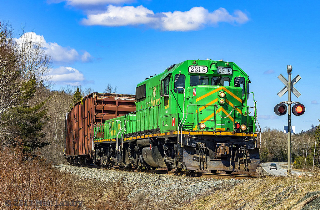NBSR 2318 and NBSR slug 008 lead a massive train of 13 loaded woodchip cars eastbound, as they head through Welsford, New Brunswick.