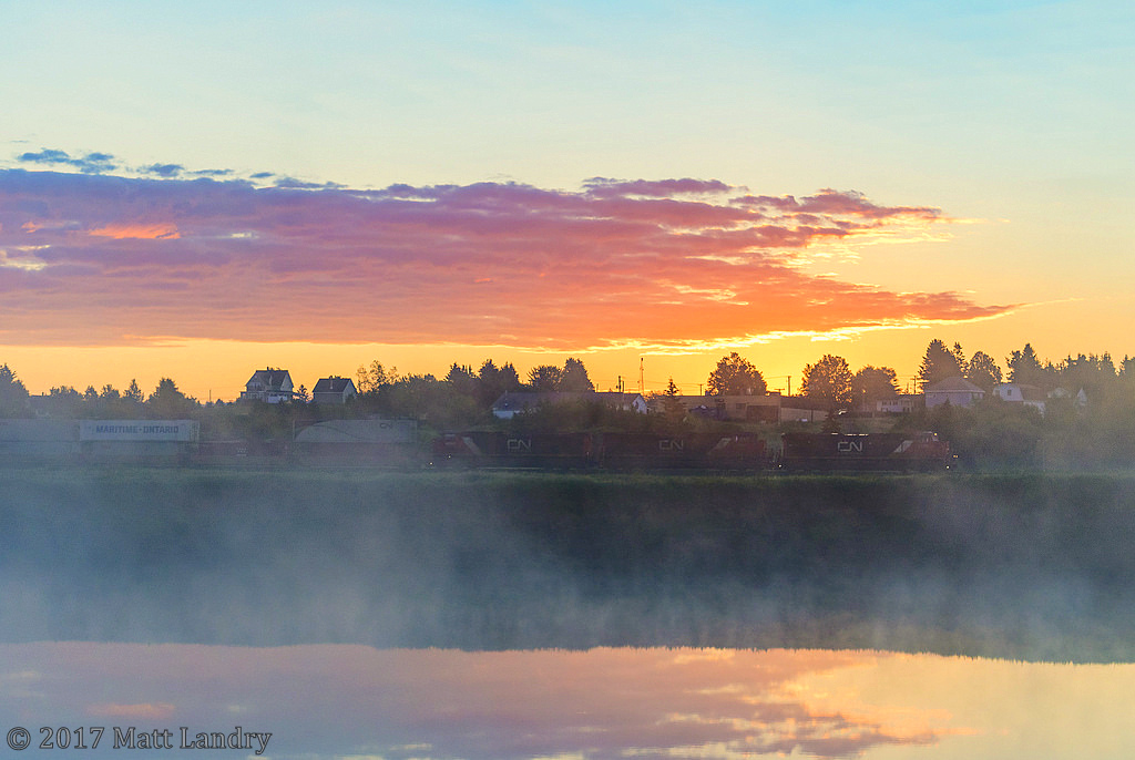 Sunrise and mist
CN eastbound stack train Q120 heads through Memramcook, New Brunswick, during a nice June sunrise. The area is also full of fog/mist coming from the marshes that run along this stretch. Kind of adds to the scene a bit.