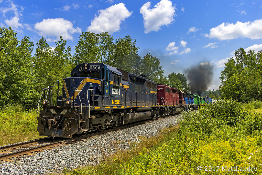 With a couple of Geeps putting up a smoke show on the rear of the consist, NBSR westbound train 907 crosses the "Dirt Road", mile 52 of the McAdam Sub.