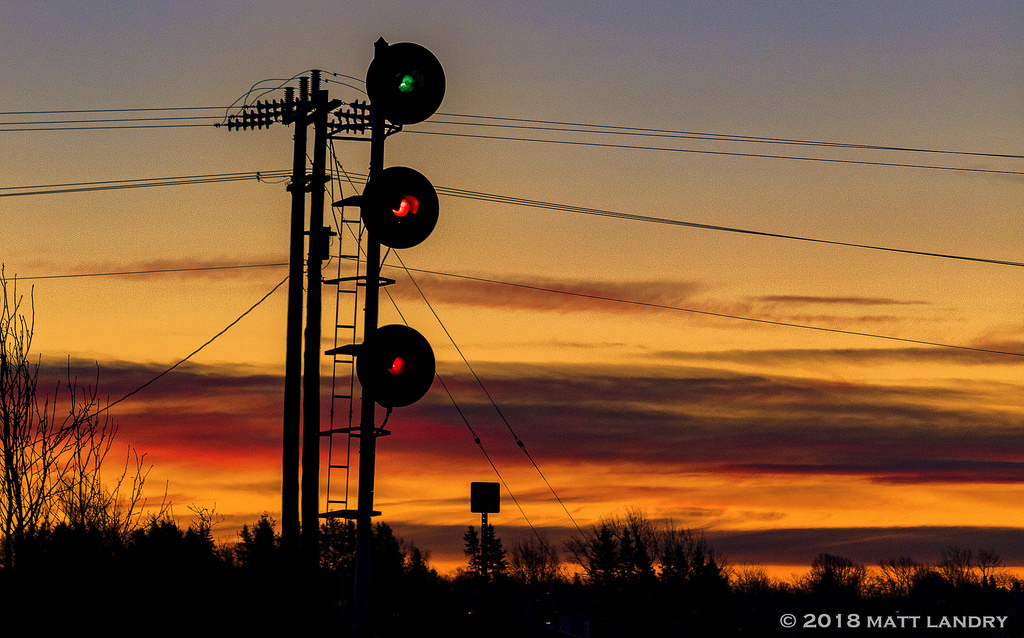 Under a fiery sunrise, the signal at the west end of Amherst is lit for CN Q120's arrival, who are a few miles away.