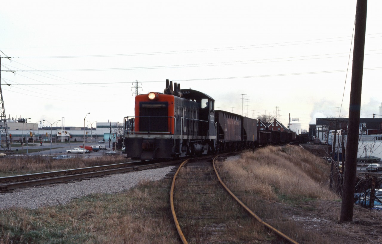 CN SW9 7000 leads the J-zone switching assignment westward along the N&NW spur in Hamilton's industrialized "north end". In the background is International Harvester's Hamilton plant which was acquired by U.S. manufacturer J I Case in 1984 and closed in 1999. The 7000 was retired in 1984 however sister units (renumbered into the 7700s) worked in Hamilton until at least 1986.