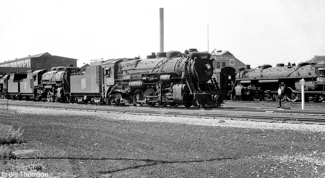 Various steam engines sit outside CN's Stratford Shops in 1959, nearing the end of their careers as dieselization on CN was almost complete. Of the units pictured, Mikado 3547 was scrapped in August 1959, Northern 6220 was scrapped July 1961, and Mikado 3257 was scrapped November 1960.