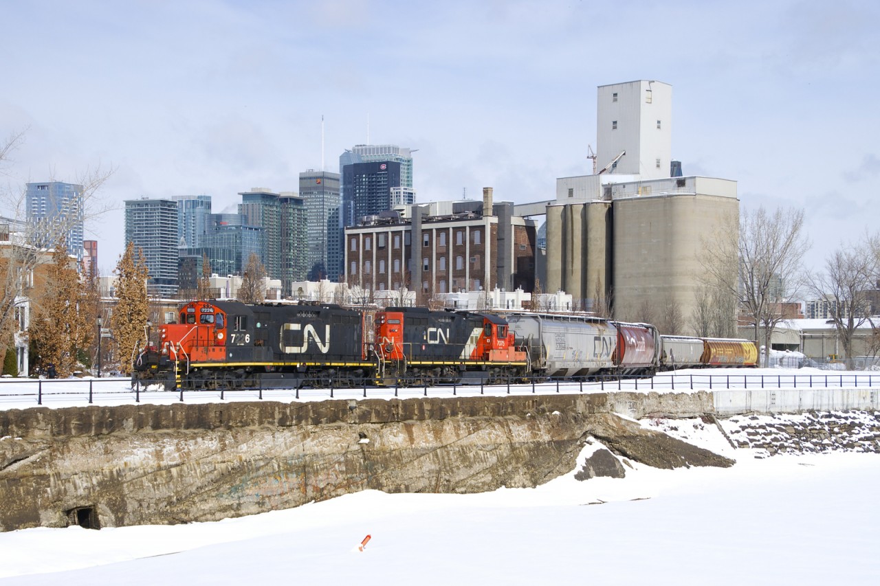 The Pointe St-Charles Switcher has GP9's CN 7226 & CN 7075 for power as it prepares to leave the Ardent Mill after picking up eight grain empties on CNs East Side Canal Bank Spur (the last client remaining on this line). In the distance at left is the skyline of downtown Montreal and in the foreground is the frozen and snow-covered Lachine Canal.