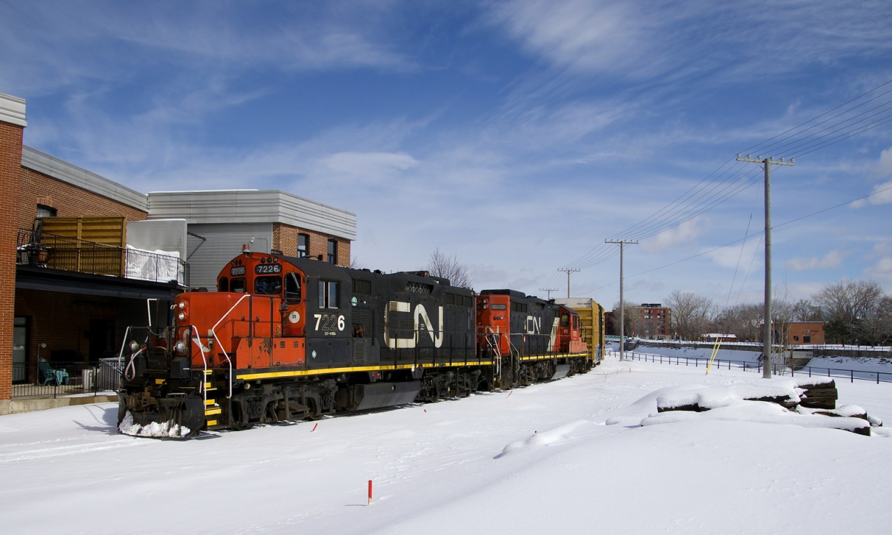 The Pointe St-Charles Switcher is stopped on the East Side Canal Bank Spur, waiting its turn to join the CN Montreal Sub. It will have to wait until intermodal train CN 120 passes. Power is GP9's CN 7226 & CN 7075.