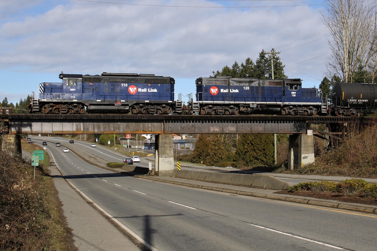 Former Burlington Northern/Northern Pacific GP9 110 and ex-CP Rail GP9u 128 lead a short train over the Trans-Canada Highway.