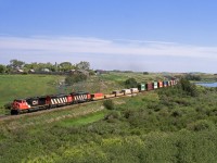 Westbound train 169 rolls through a coulee between Neola siding and crew change point of Biggar. CP's parallel Wilkie Sub. is on the top of the valley behind the farmyard